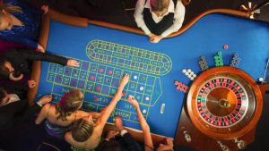 Vista desde arriba: Lujoso Casino Invitados masculinos y femeninos ponen fichas de apuestas en una mesa de juego, tratando de predecir el resultado de un juego de ruleta.